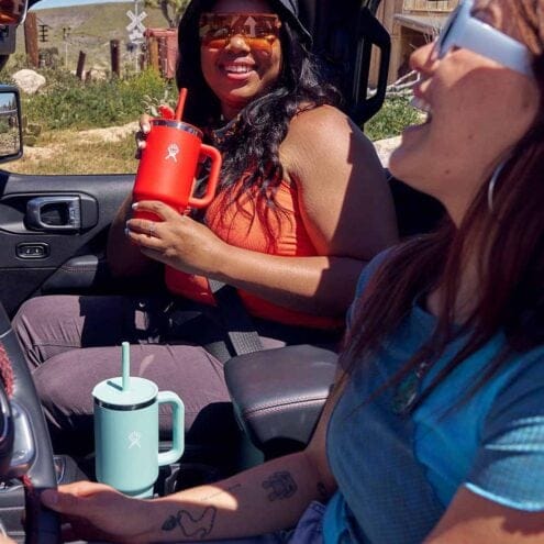 två modeller har varsin En stor och praktisk Hydro Flask All Around Travel Tumbler med sugrör 32oz/946ml i en bil