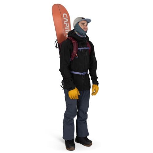 en man bär en Osprey Glade 12 skidryggsäck (unisex) med en snowboard