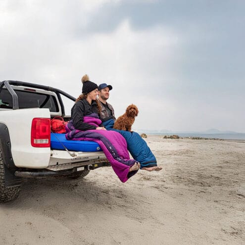 två människor och en hund sitter på ett Sea To Summit Selfinflate Mat Comfort Deluxe Wide självuppblåsbart liggunderlag